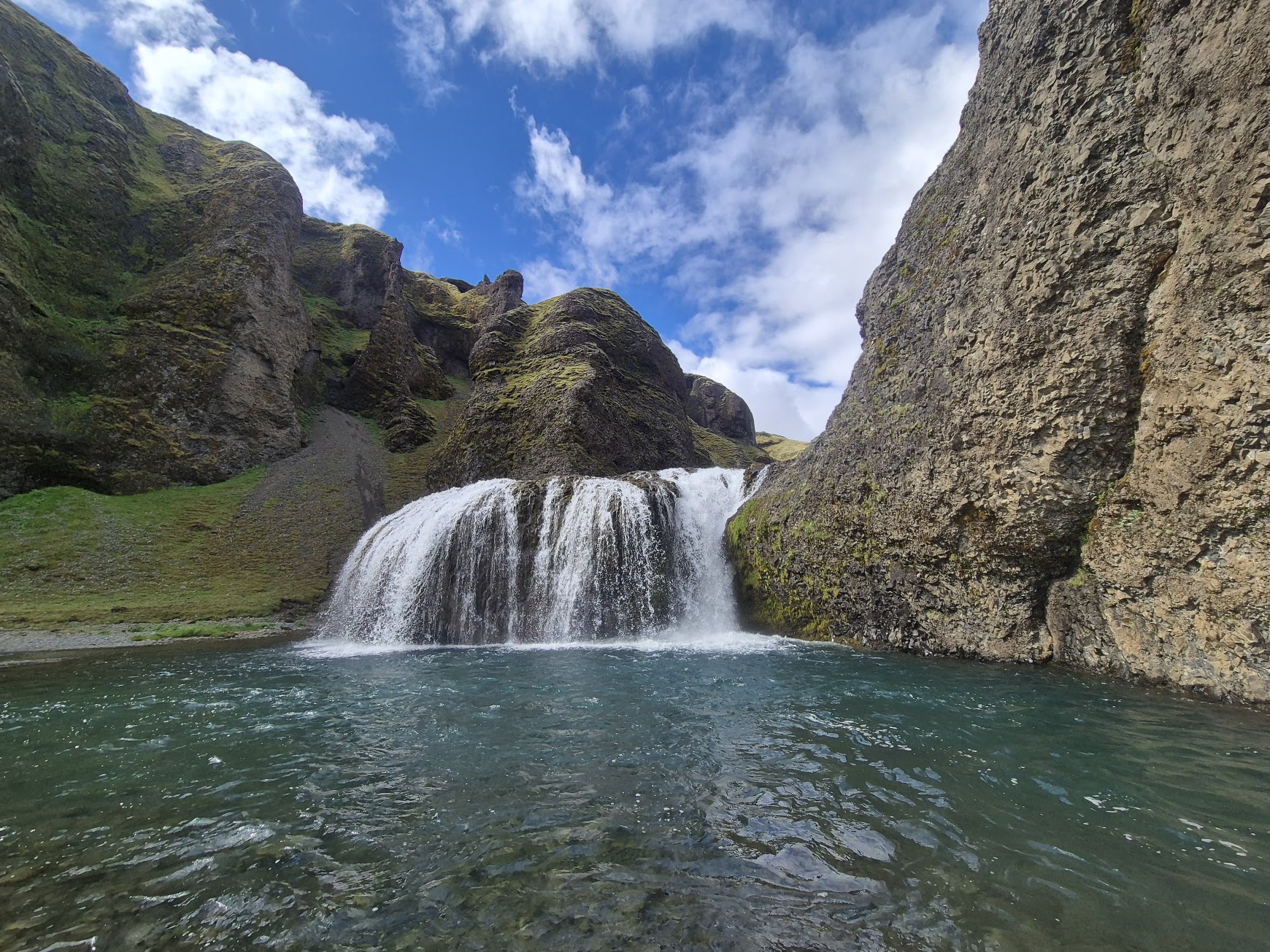 Stjórnarfoss waterfall cascading into a turquoise pool under blue Icelandic sky